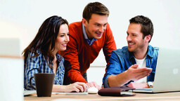Three colleagues collaborating around a laptop during a team meeting